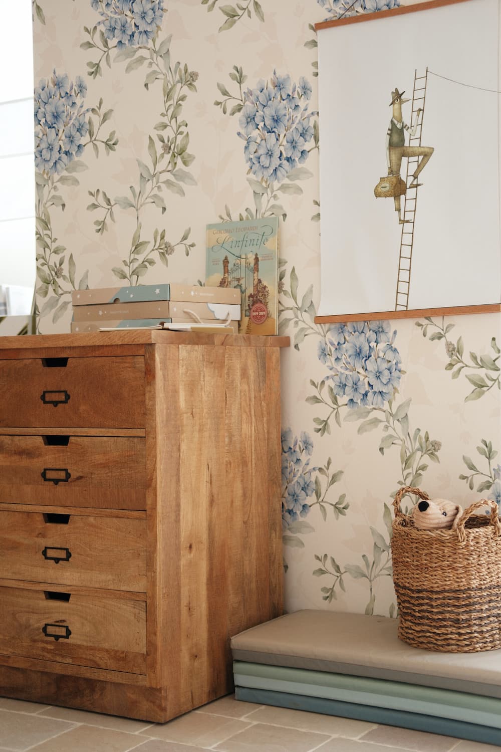 Wooden dresser against floral wallpaper with a wicker basket on a bench.
