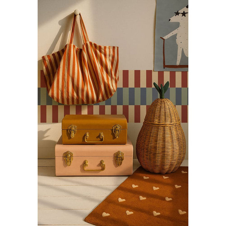 Striped bag hanging on a wall with suitcases and a woven vase on a wooden floor.