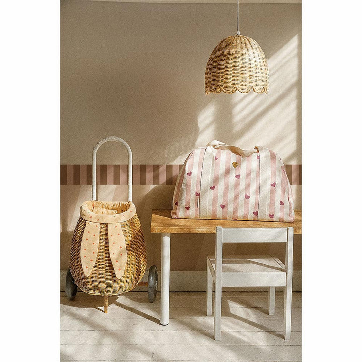 Wicker basket with bunny ears and striped bag on a wooden table in a room with a wicker pendant light.