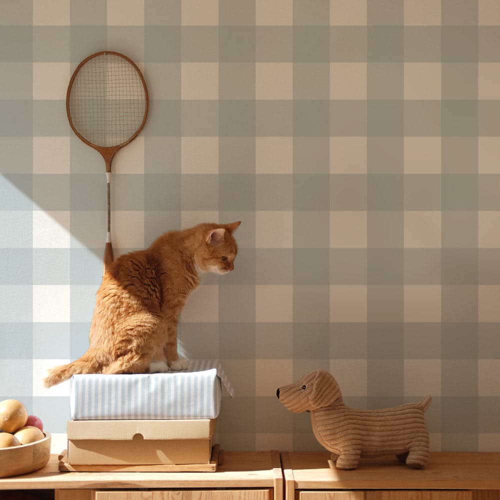 Cat sitting on a box with a badminton racket against a checkered wall, next to a dog figurine.