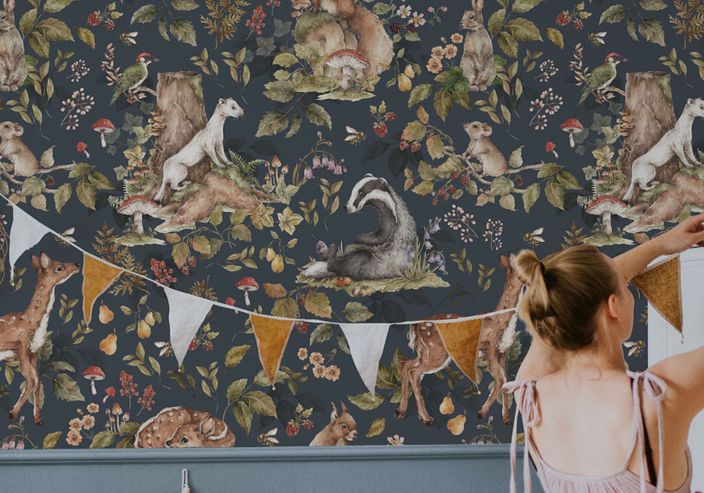 Woman standing in front of a wall with animal-themed wallpaper and bunting flags.
