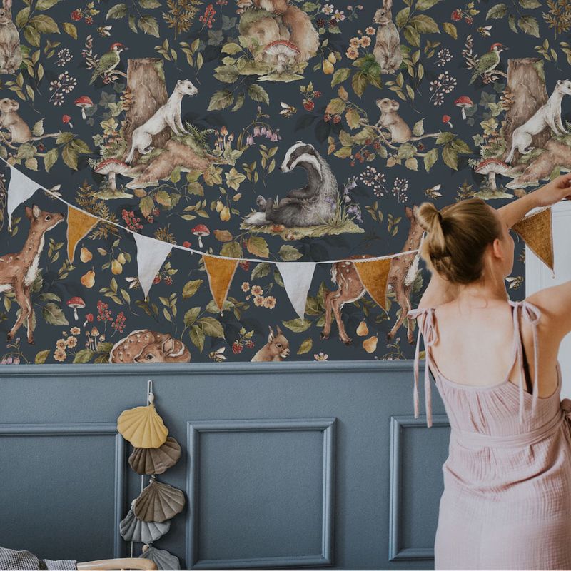 Woman standing in front of a wall with nature-themed wallpaper featuring animals and bunting.