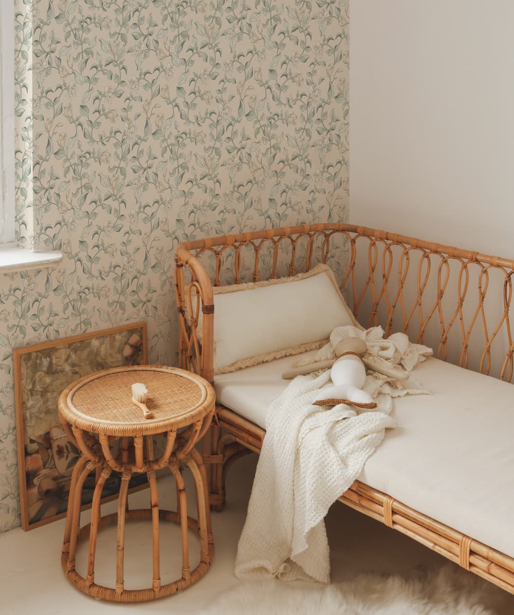 Rattan daybed with white cushions and a small round table against floral wallpaper.