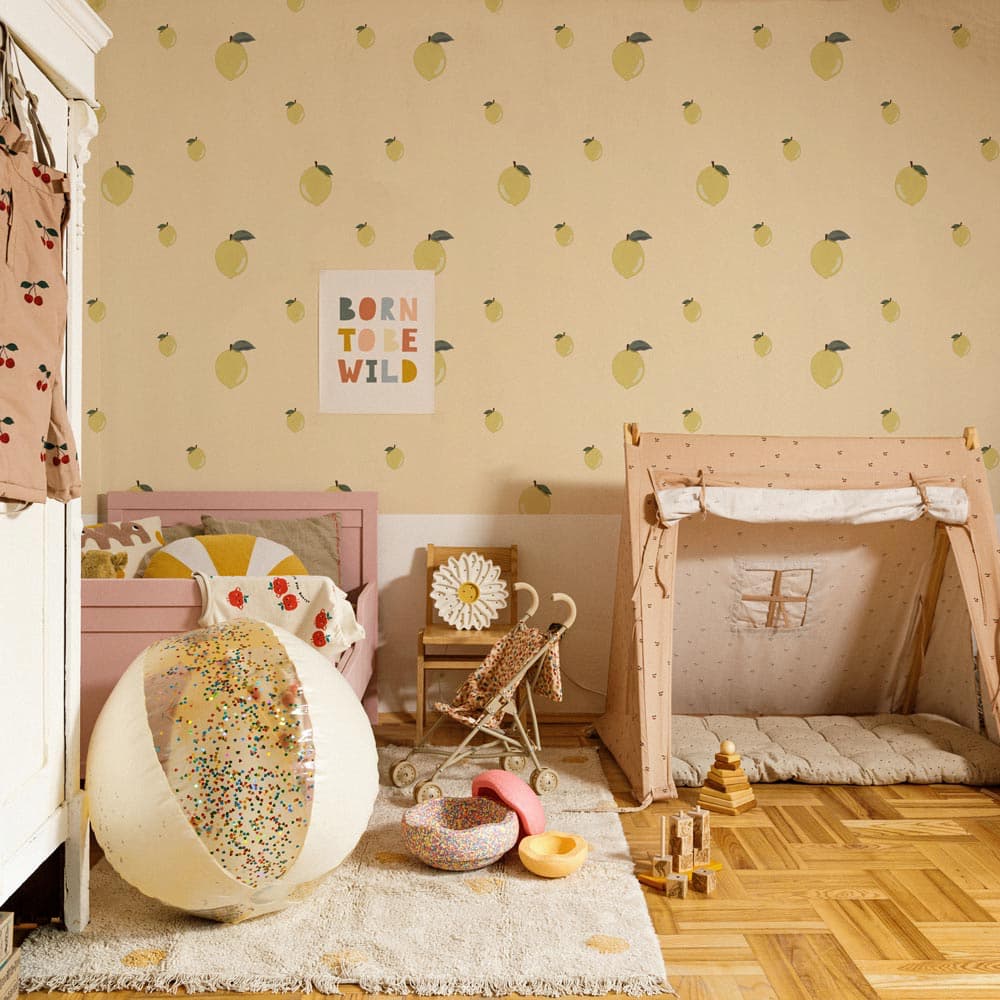 Children's room with a pink bed, wooden playhouse, and decorative elements on a wall with fruit pattern.