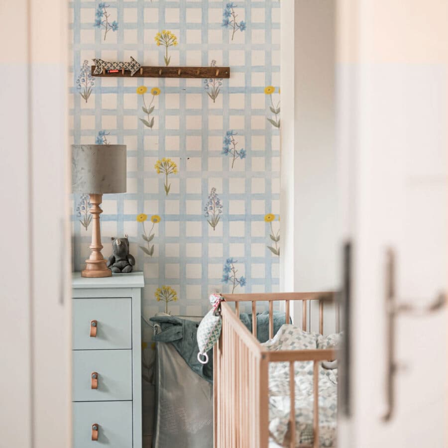 Nursery room with floral and check wallpaper, crib, and dresser.