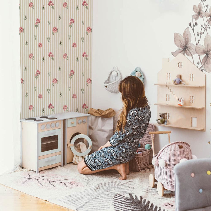 Child playing with toys in a room with floral wallpaper and wooden furniture.