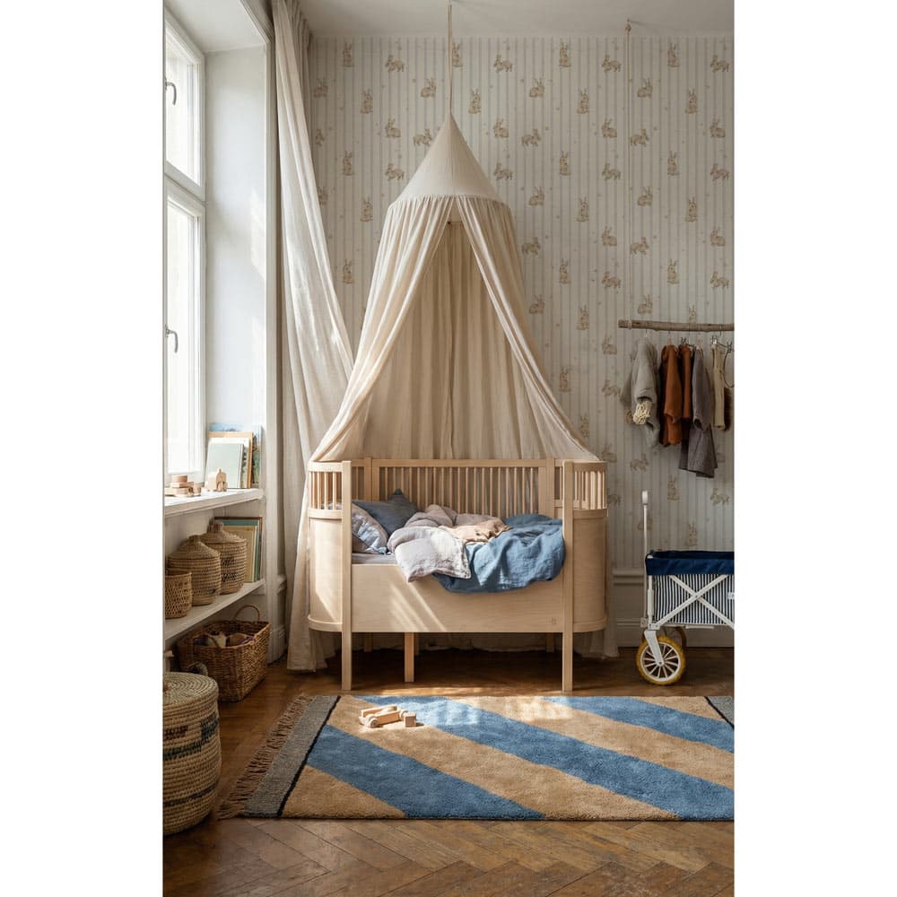 Children's room with a wooden crib, canopy, and patterned wallpaper.