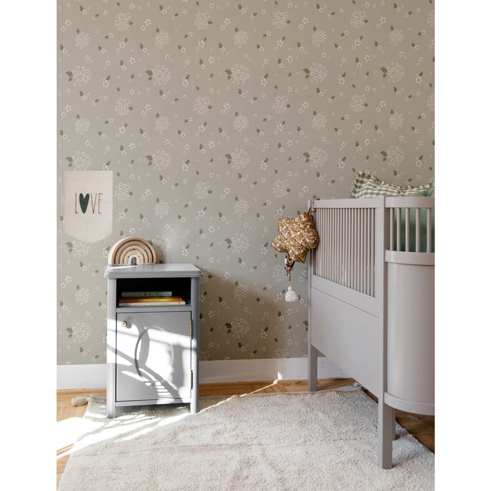 Nursery room with crib and side table against a floral patterned wallpaper.
